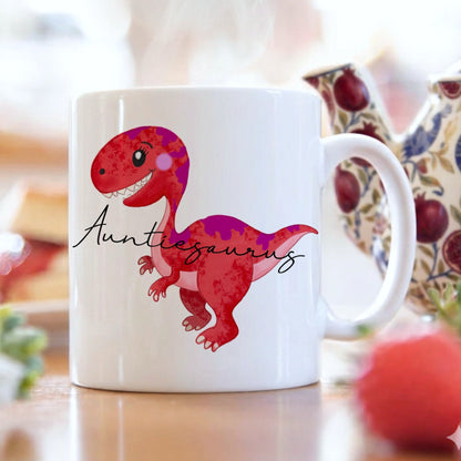 White mug with a red dinosaur illustration and 'Auntiesaurus' text on a blurred background