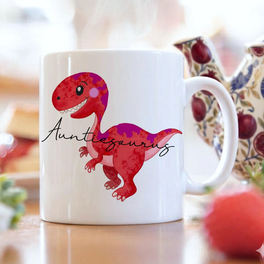 White mug with a red dinosaur illustration and 'Auntiesaurus' text on a blurred background