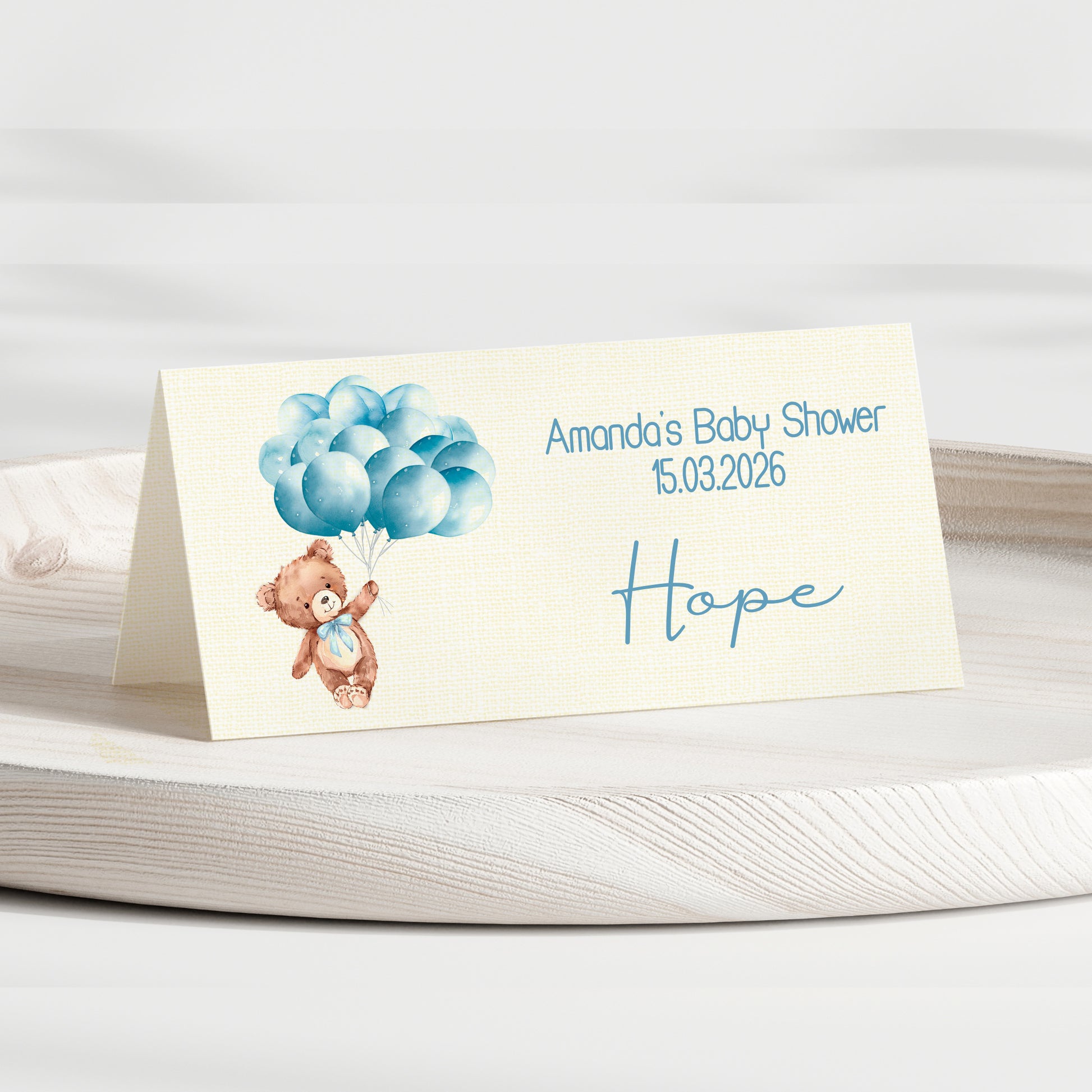 Baby shower invitation card with teddy bear and balloons on a white surface