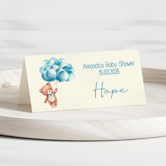 Baby shower invitation card with teddy bear and balloons on a white surface