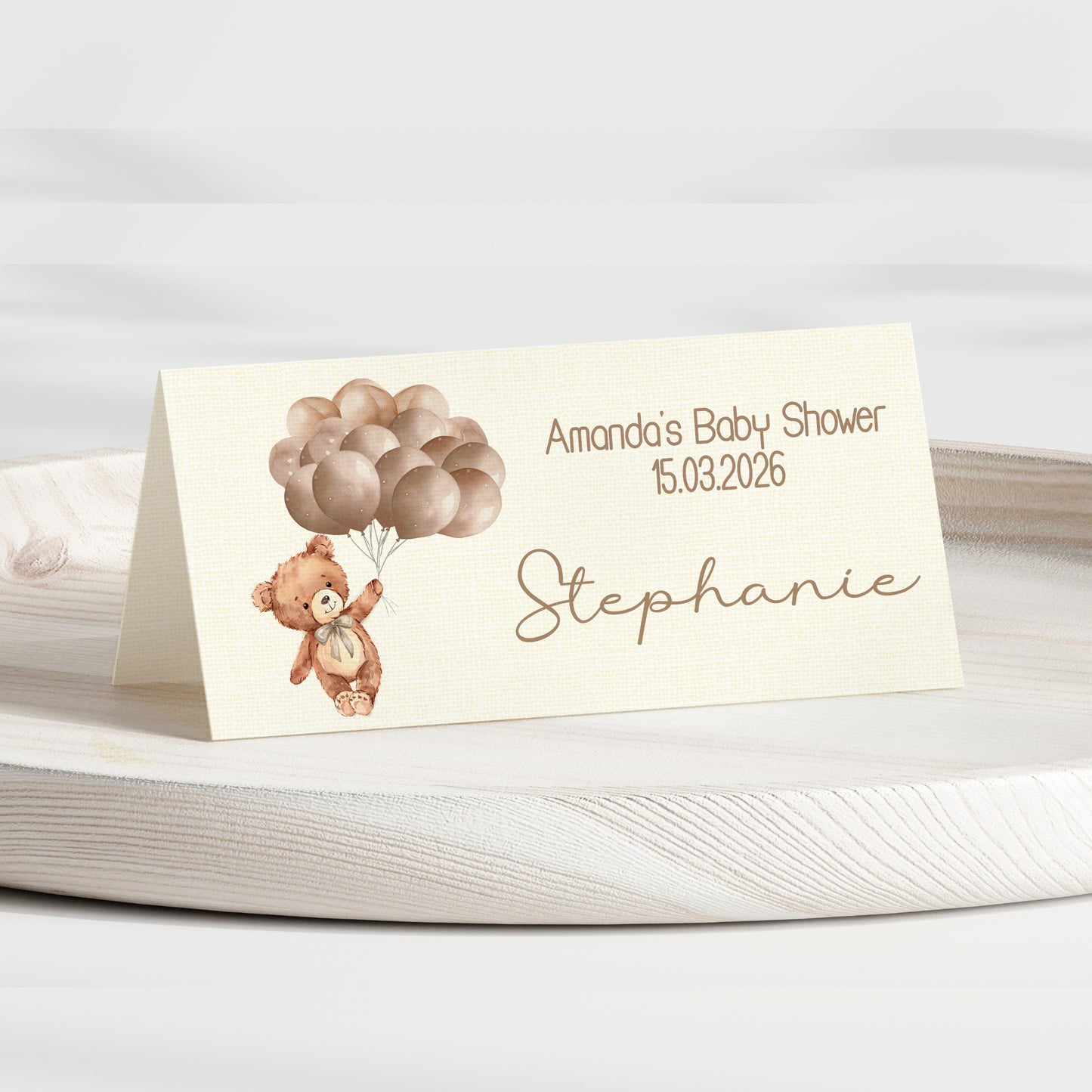 Baby shower invitation card with teddy bear and balloons on a white surface