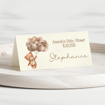 Baby shower invitation card with teddy bear and balloons on a white surface