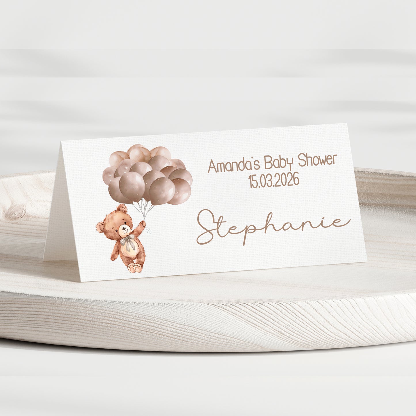 Baby shower place card with teddy bear and balloons on a white surface