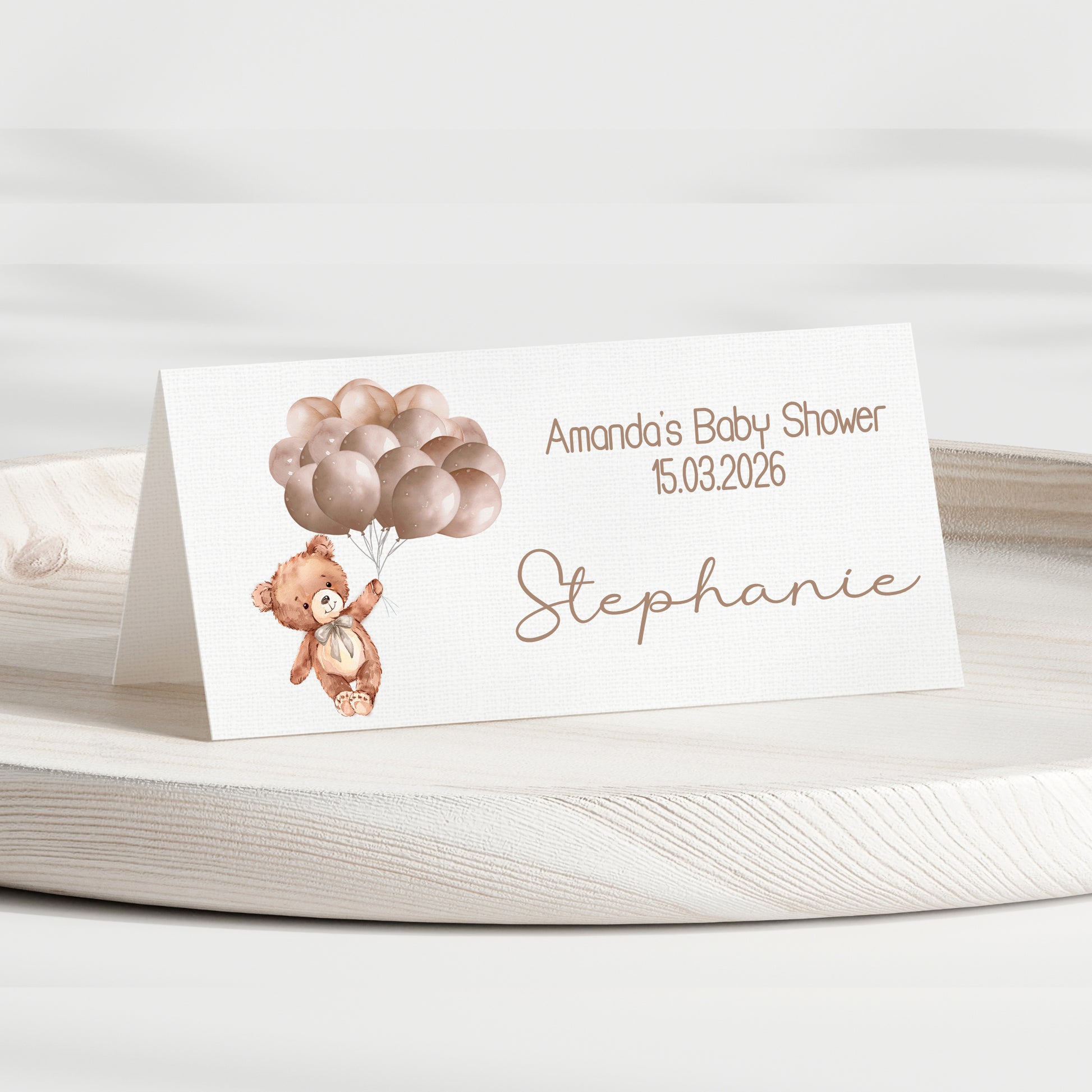 Baby shower place card with teddy bear and balloons on a white surface