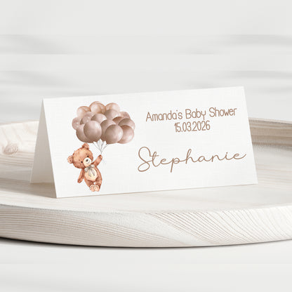 Baby shower place card with teddy bear and balloons on a white surface