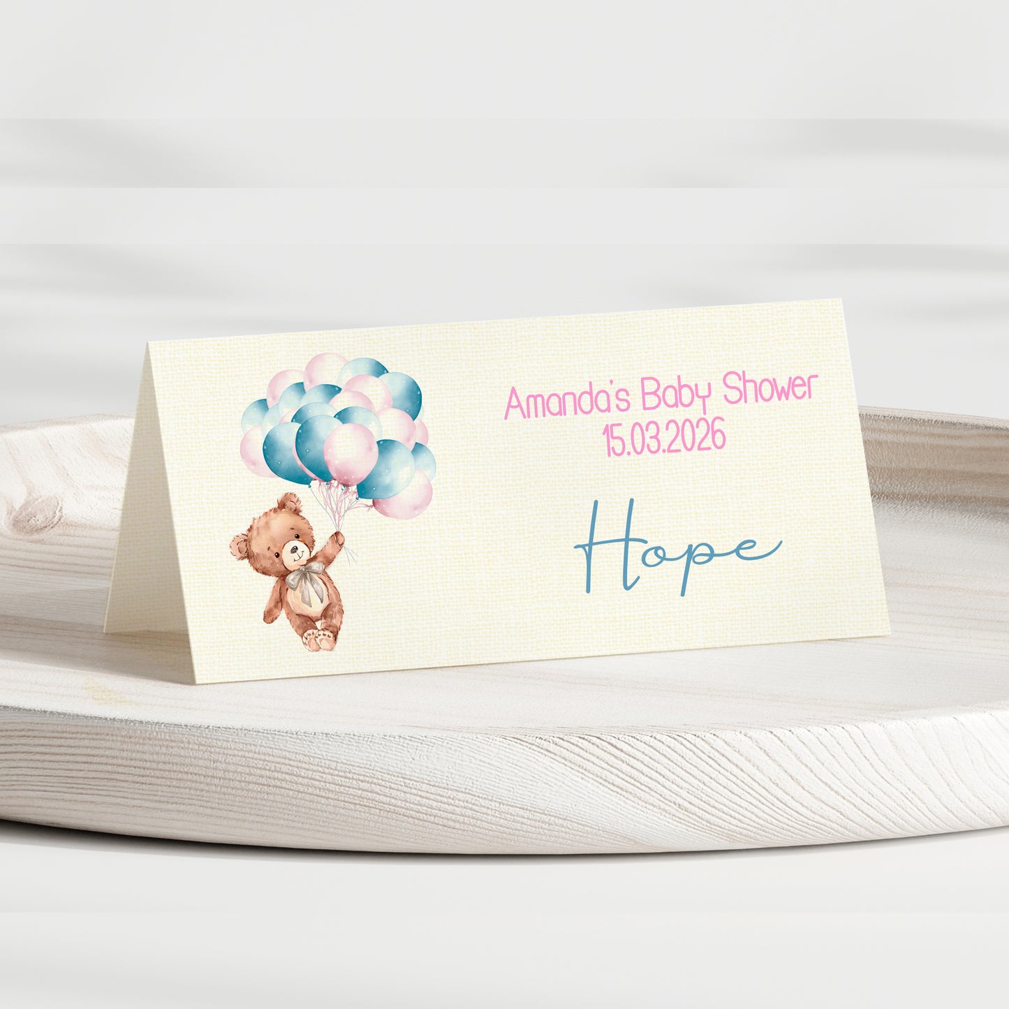 Baby shower invitation card with teddy bear and balloons on a white surface