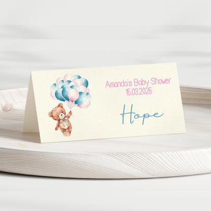 Baby shower invitation card with teddy bear and balloons on a white surface