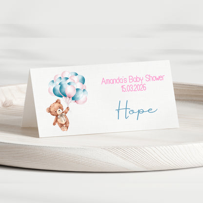 Baby shower invitation card with teddy bear and balloons on a white surface