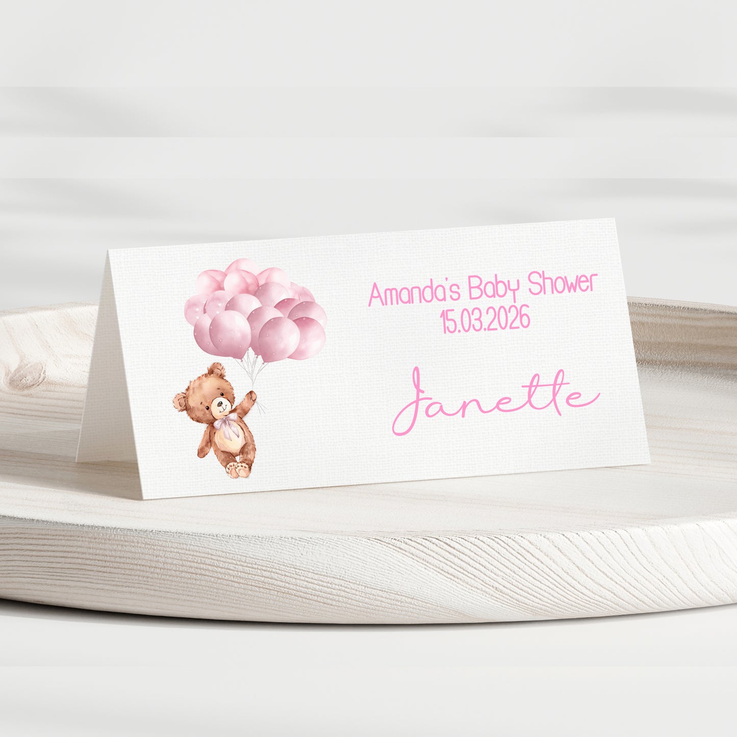Baby shower invitation card with teddy bear and balloons on a white surface
