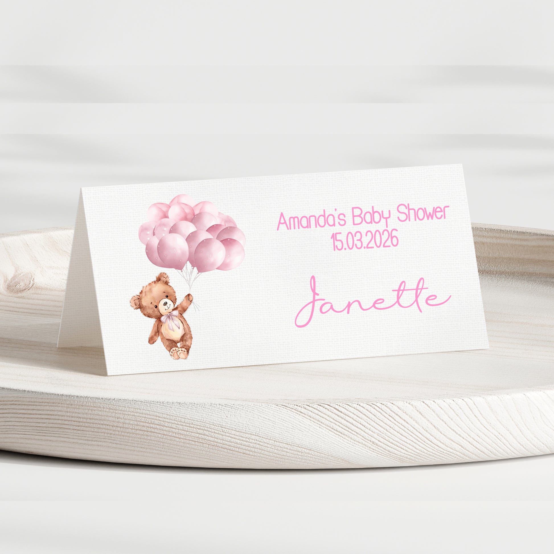 Baby shower invitation card with teddy bear and balloons on a white surface