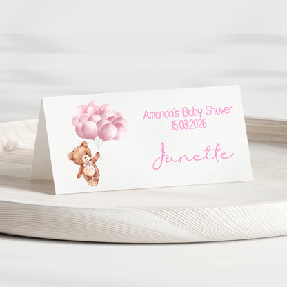 Baby shower invitation card with teddy bear and balloons on a white surface
