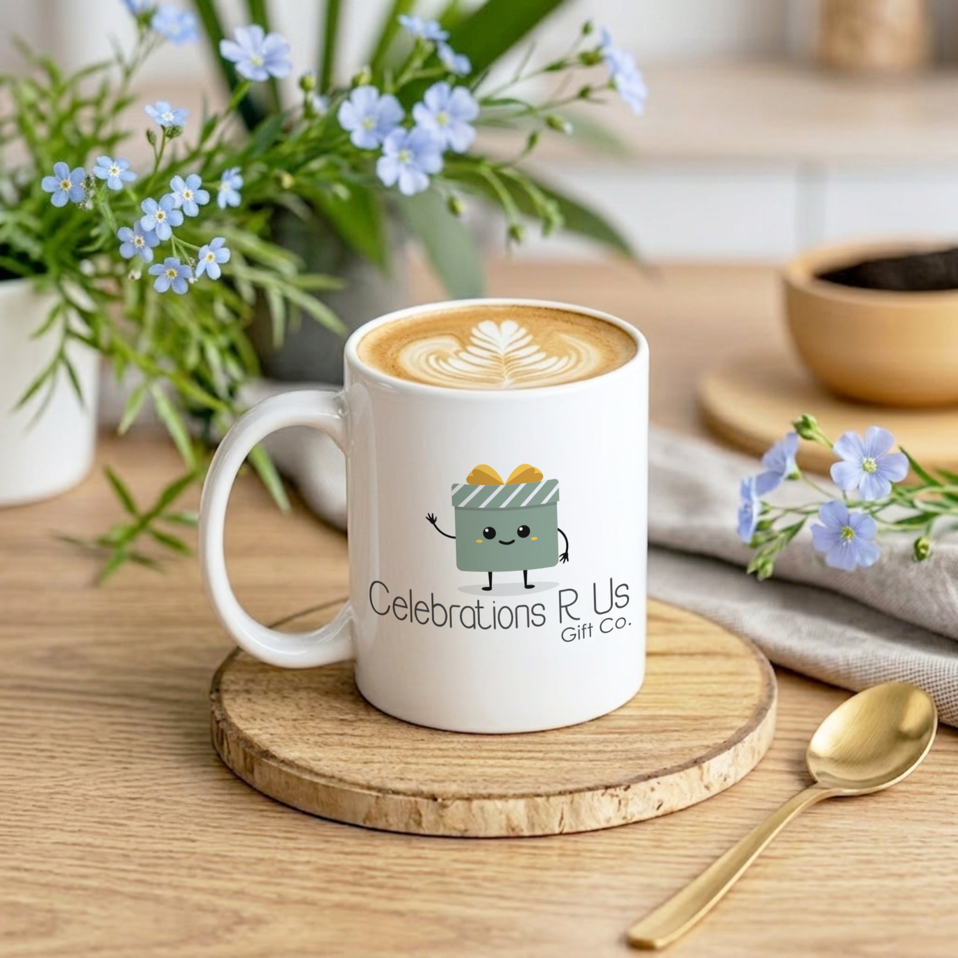 White mug with 'Celebrations R Us' logo on a wooden coaster with flowers and a spoon in the background