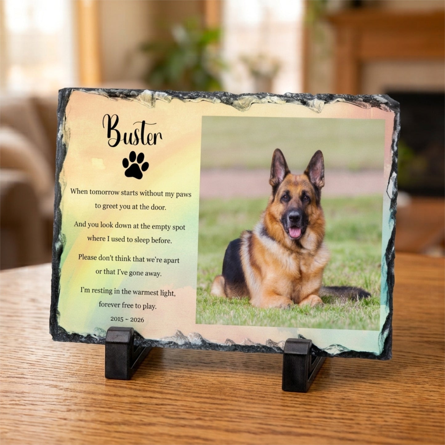 Personalised memorial slate plaque on a small black stand, featuring a photo of a German Shepherd dog and a memorial poem titled 'Buster' with a paw print, displayed on a wooden surface.