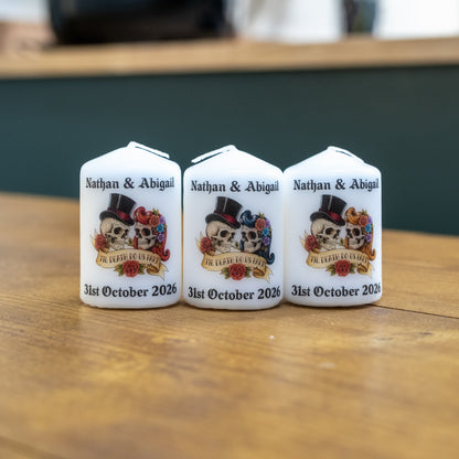 Three personalised white wedding candles with sugar skull designs, displayed on a wooden table.