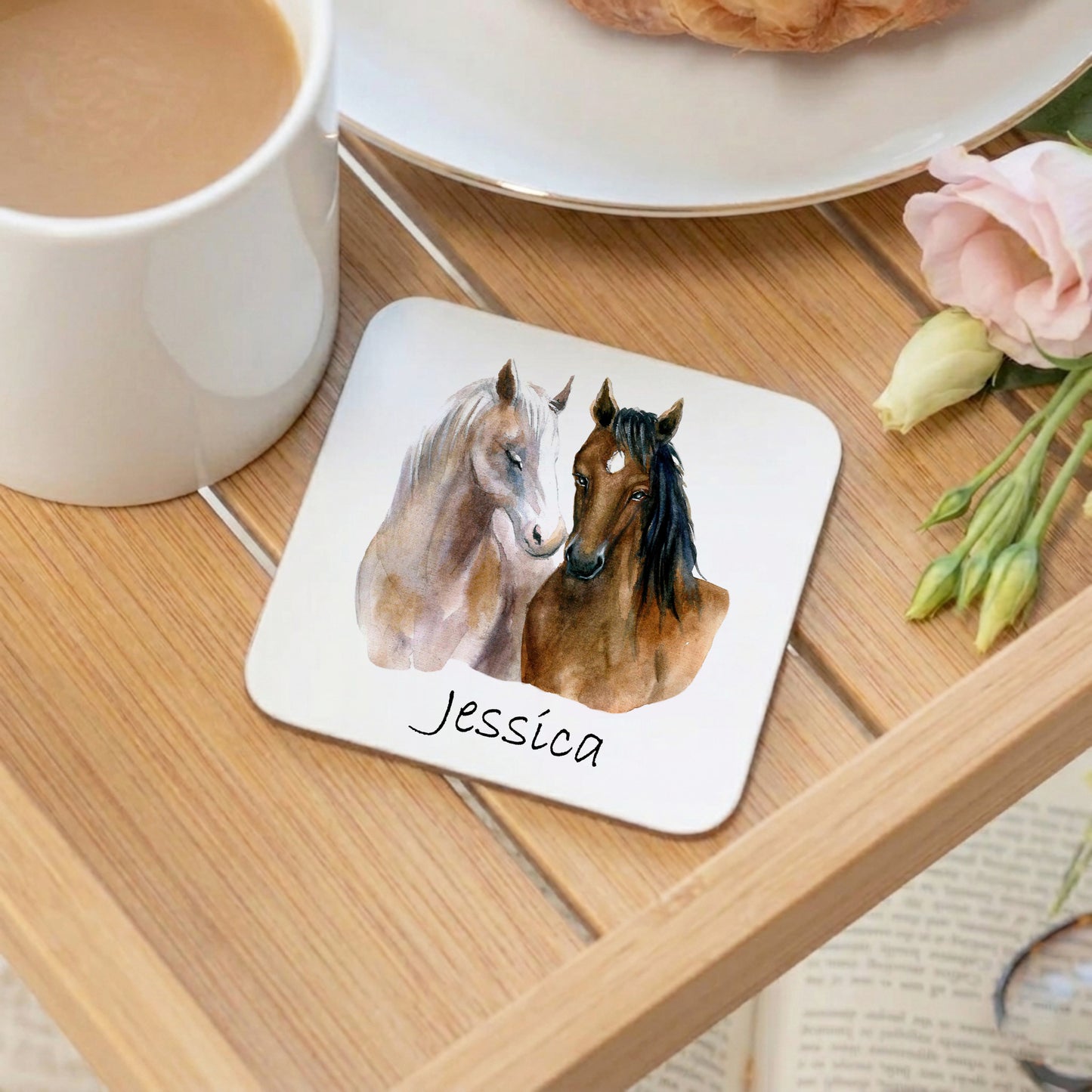 Coaster with two horses and the name 'Jessica' on a wooden table with a cup of coffee and flowers.