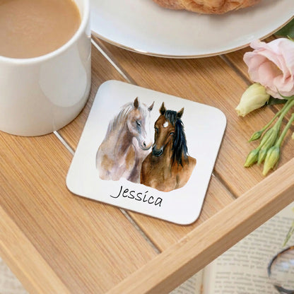 Coaster with two horses and the name 'Jessica' on a wooden table with a cup of coffee and flowers.