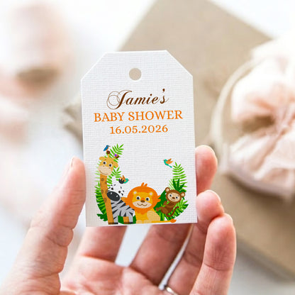 Hand holding a baby shower invitation tag with cartoon animals and text.