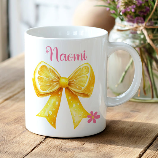 White mug with a yellow bow design with any name on a wooden surface with flowers in the background