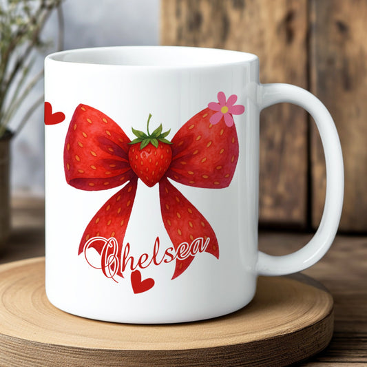White mug with strawberry bow design and 'Chelsea' text on a wooden coaster.