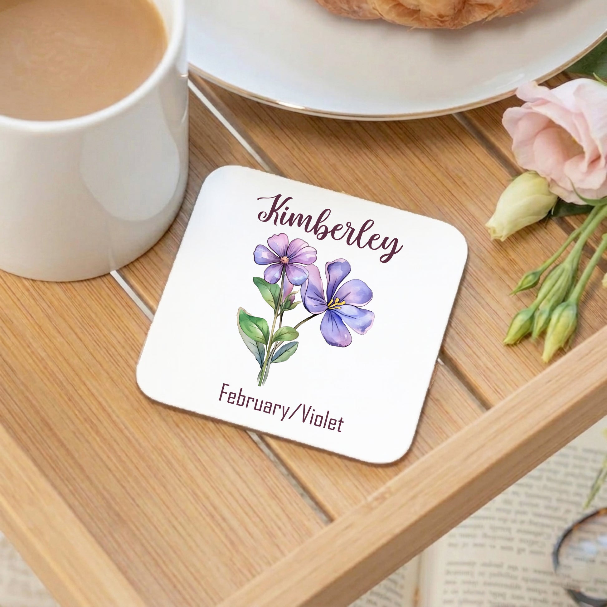 Coaster with floral design and text on a wooden table with a cup of coffee and flowers.
