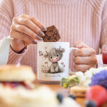 Person holding a mug with a cute animal design and a cookie, sitting at a table with food.