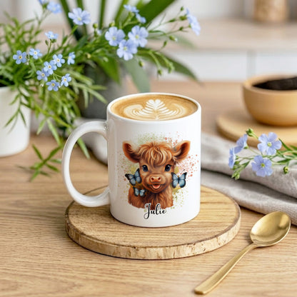 White mug with a cow illustration and 'Julie' text on a wooden coaster with flowers and a spoon.