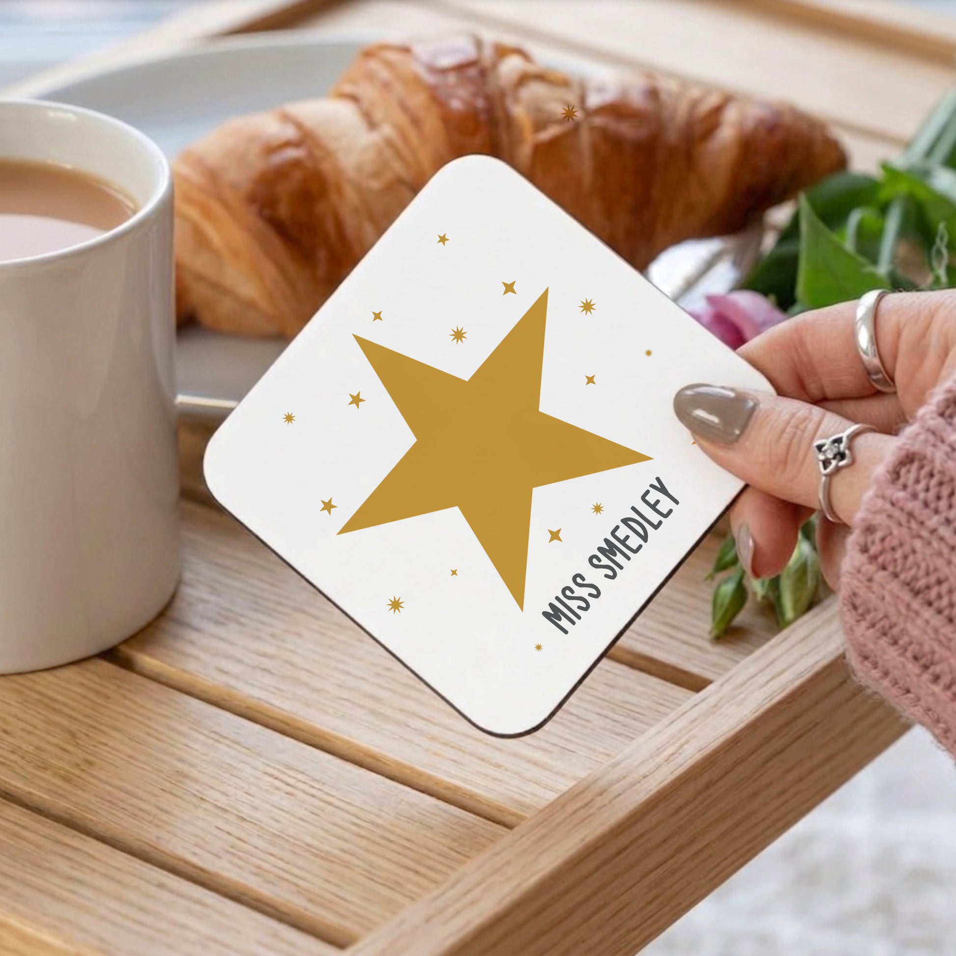 Coaster with star design held by a hand on a table with coffee and croissants.