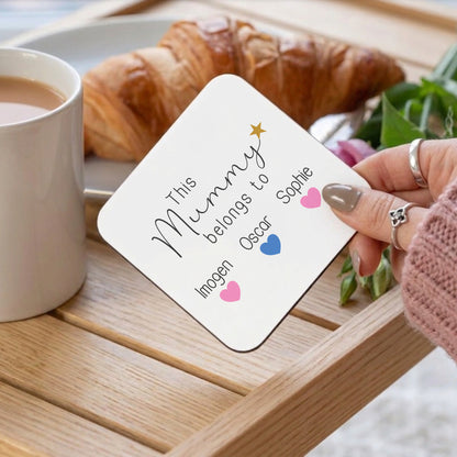 Person holding a card with 'This Mummy belongs to' text on a table with a croissant and coffee.