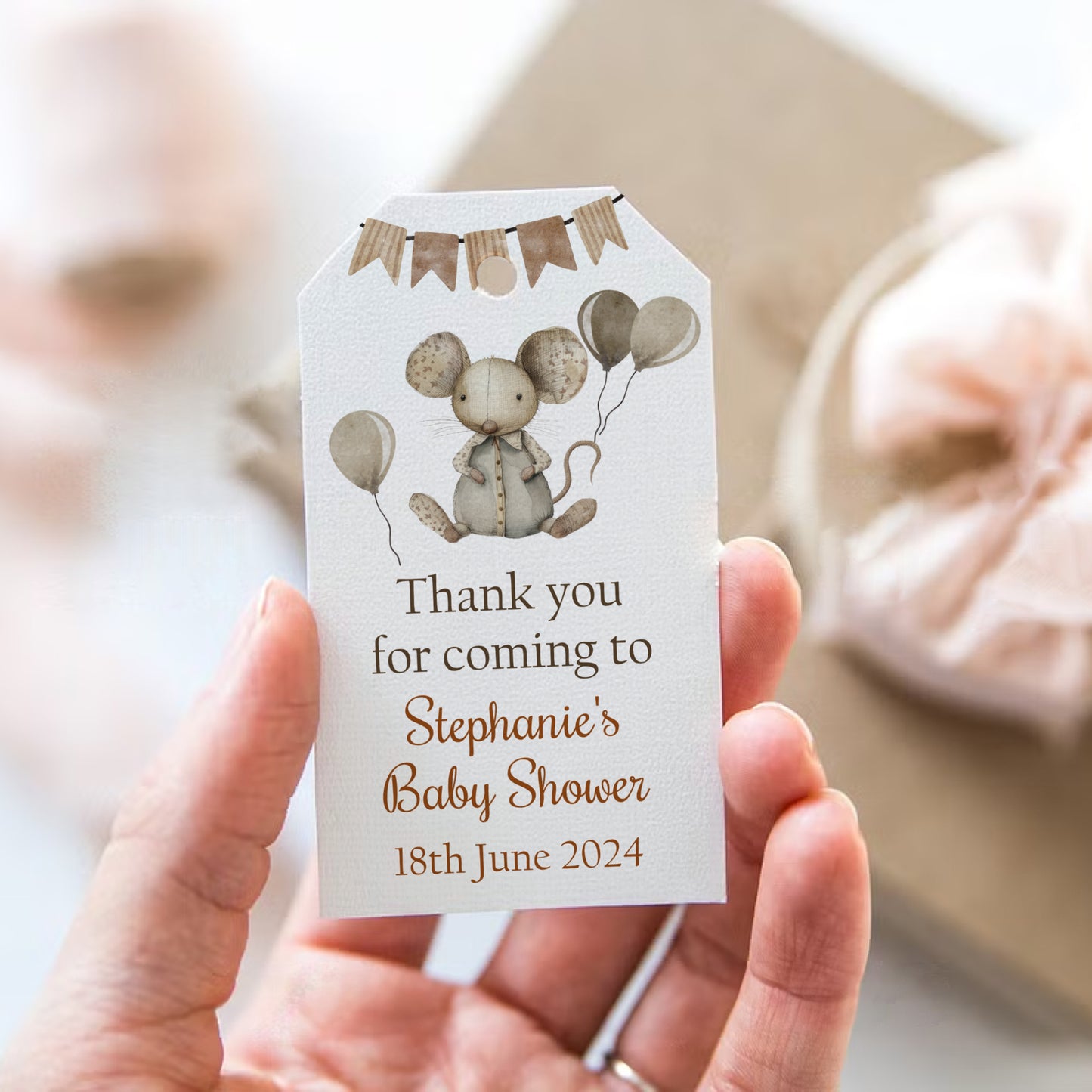 Baby shower favor tag with mouse illustration and personalized text held by a hand.