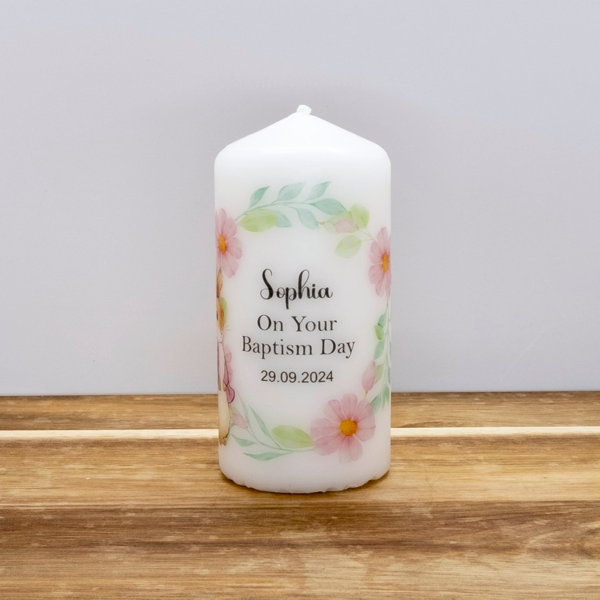 Decorative candle with floral design and text on a wooden surface