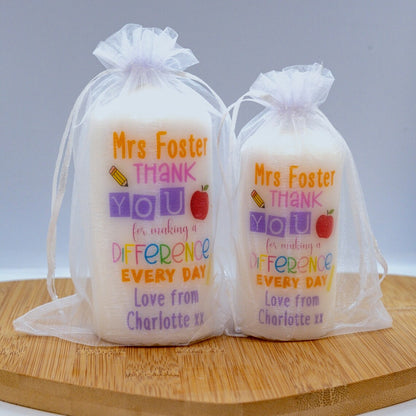 Two personalised candles with printed text 'Mrs Foster THANK YOU for making a DIFFERENCE every day' with additional personalized text that reads 'Love from Charlotte xx'. The candles are placed in transparent packaging.