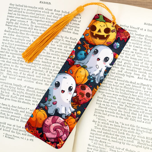 Colorful Halloween-themed bookmark with ghosts, pumpkins, and candy on a book page.