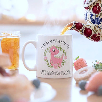 Mug with 'Mummysaurus' design being filled with tea, surrounded by food and a jar of honey.