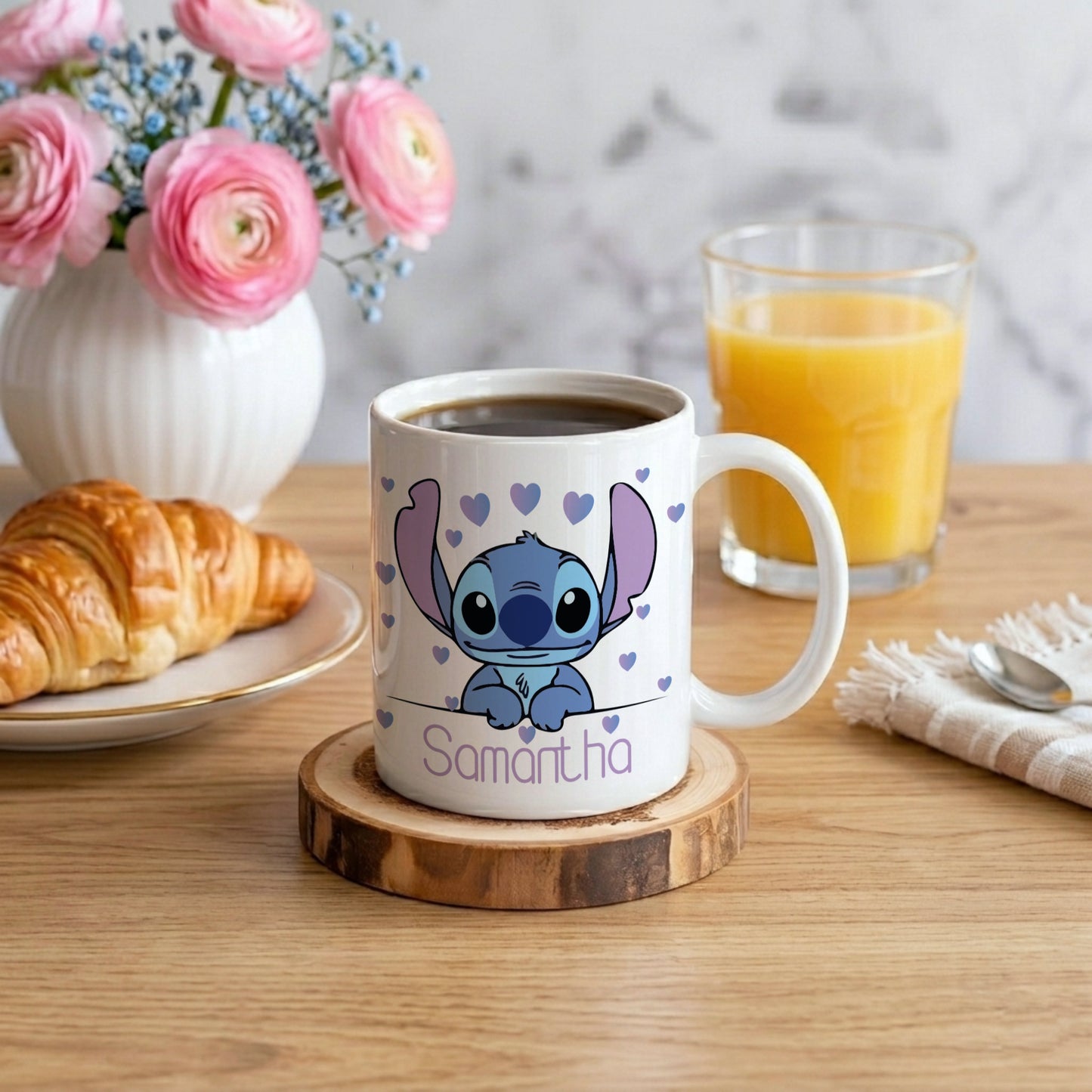 Mug with cartoon character design on a wooden table with coffee, orange juice, and flowers.
