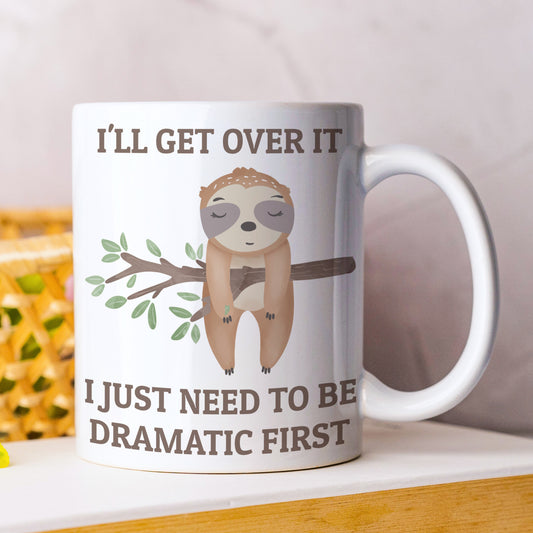 Mug with sloth illustration and humorous text on a white surface