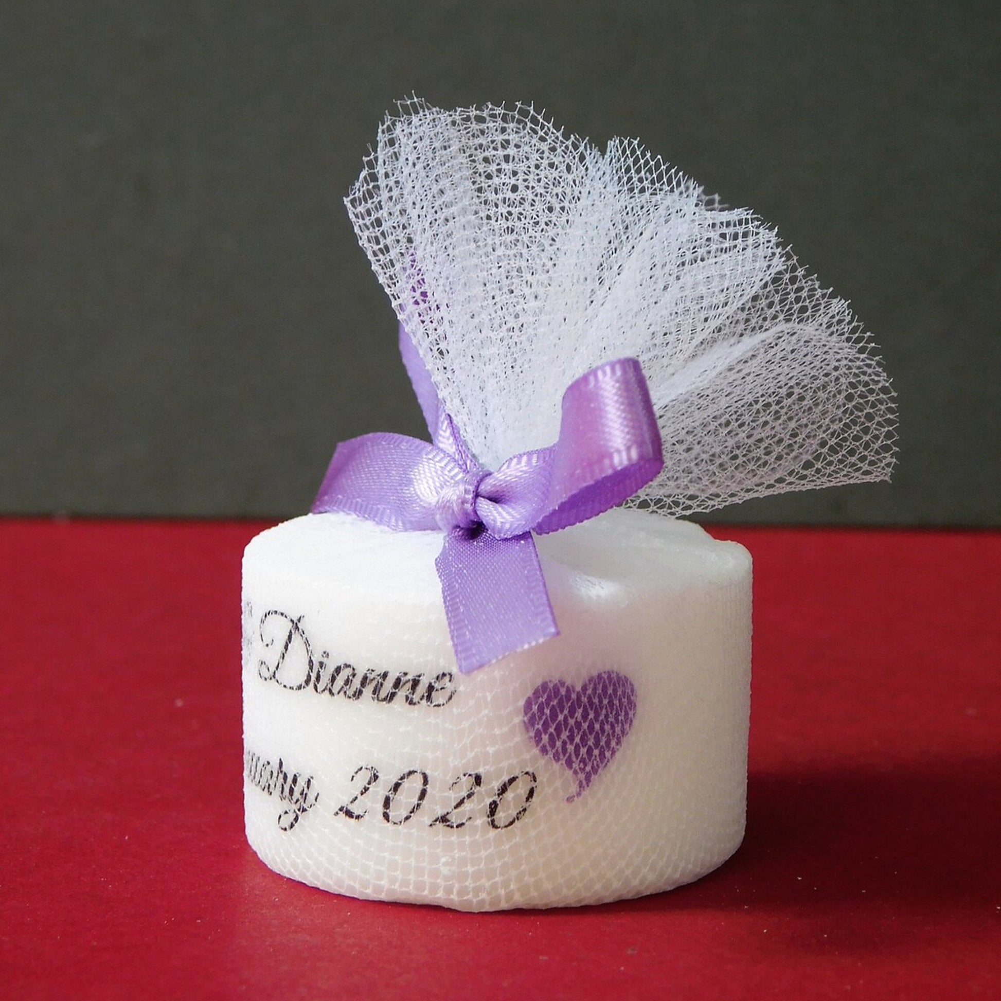 Small white candle with a purple ribbon and mesh on a red surface