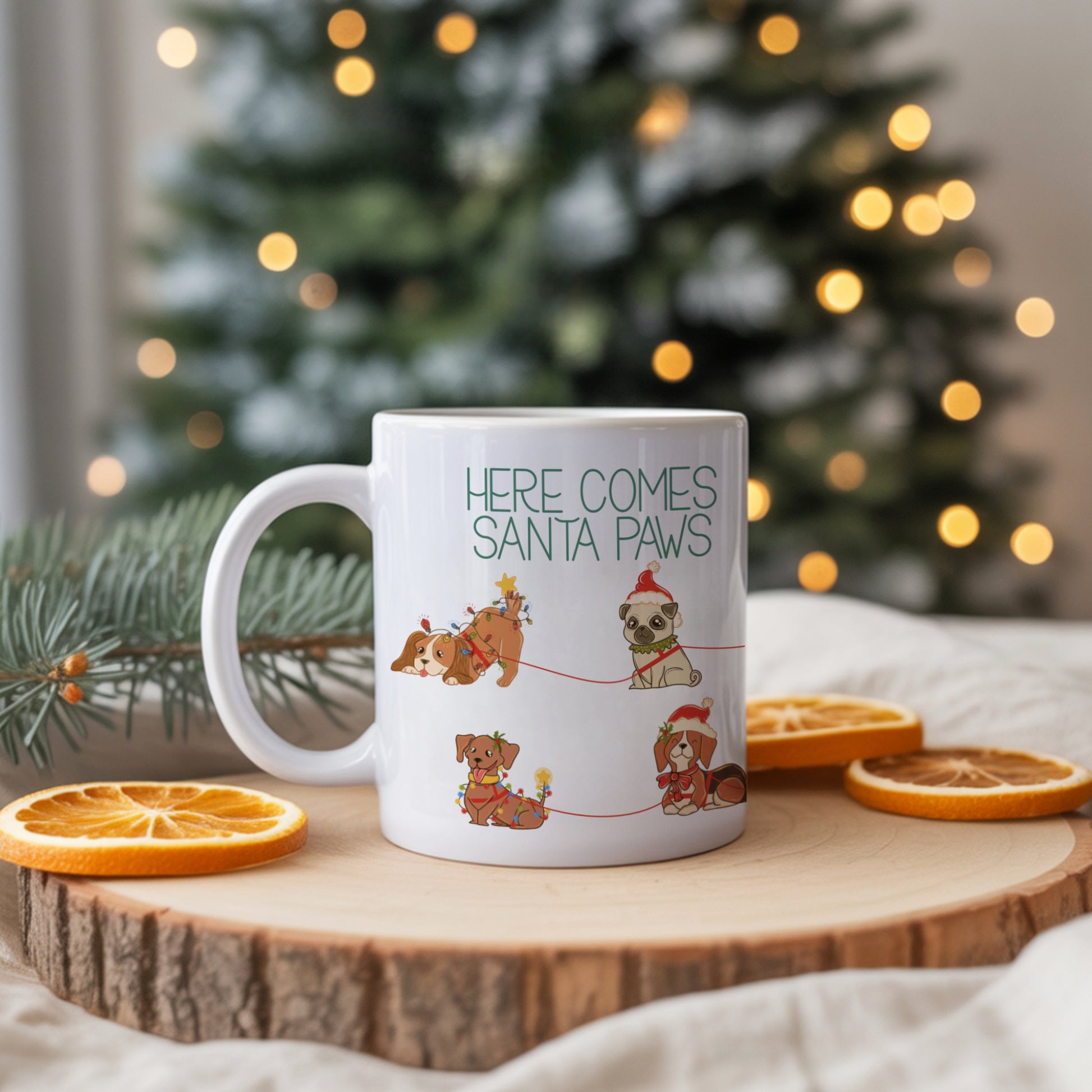 White mug with 'Here Comes Santa Paws' text and dog illustrations on a wooden surface with Christmas decorations.