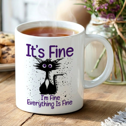White mug with a black cat illustration and text on a wooden table with cookies and flowers.