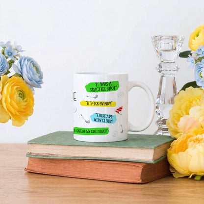 A white ceramic mug with colourful text and illustrations sits on a stack of two old books on a wooden table, styled with yellow and blue flowers and a glass candlestick holder against a white background.