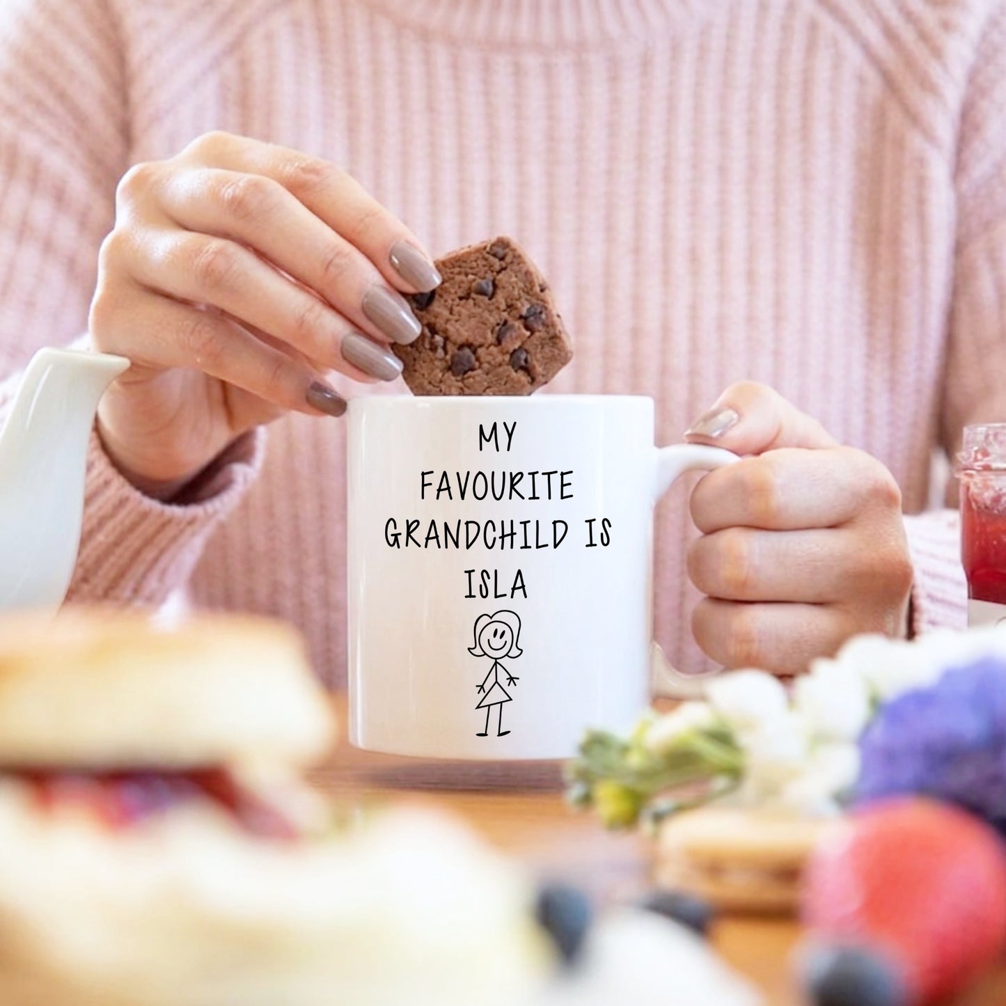 A woman dunking a biscuit into a cup which has the text My favourite Grandchild is Isla