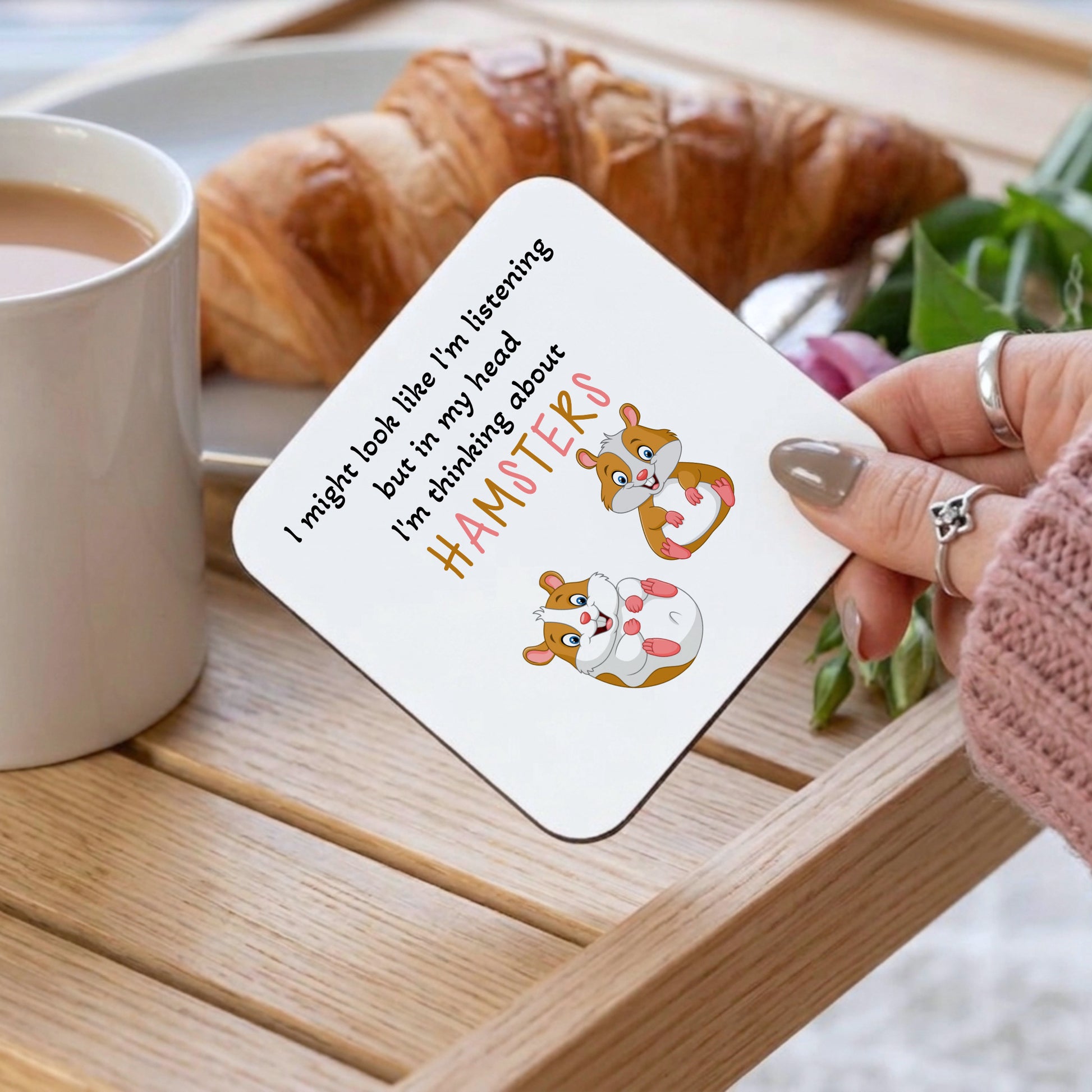 Coaster with cartoon hamsters and humorous text on a table with a croissant and coffee.