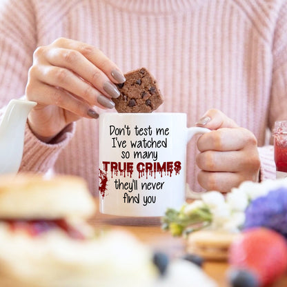 Person holding a mug with text and a cookie, sitting at a table.