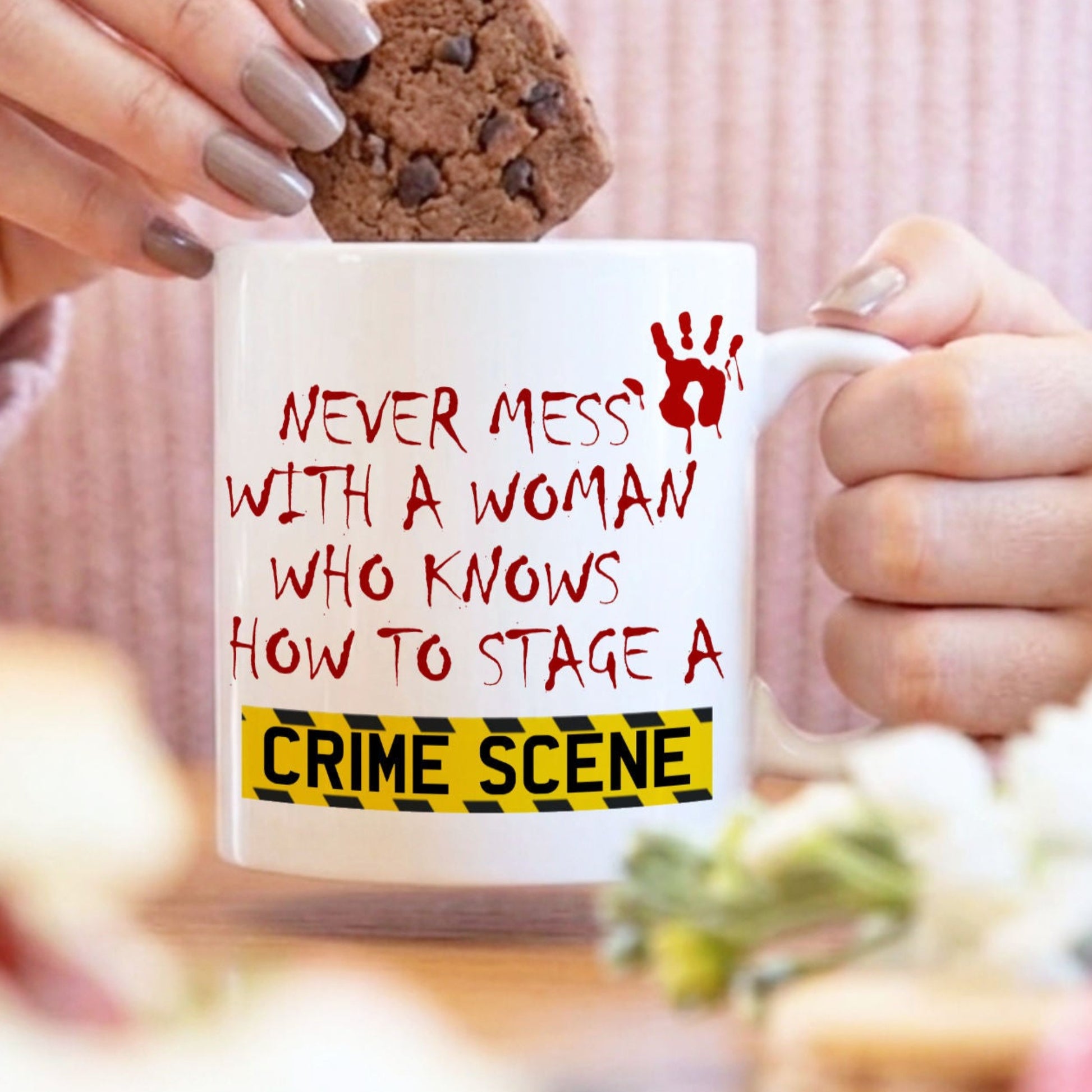 Person holding a mug with text and a cookie, blurred background