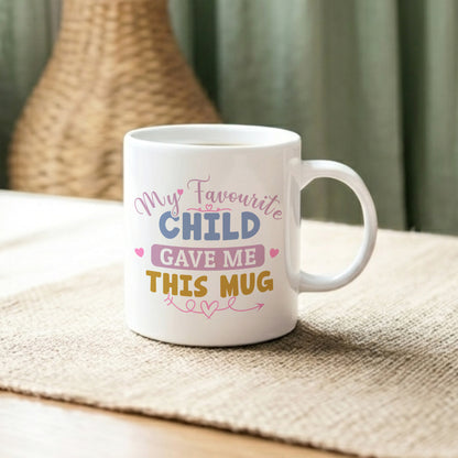 My Favourite Child Gave Me This Mug' white ceramic mug with colourful typography and pink heart details, displayed on a linen surface with a wicker vase in the background
