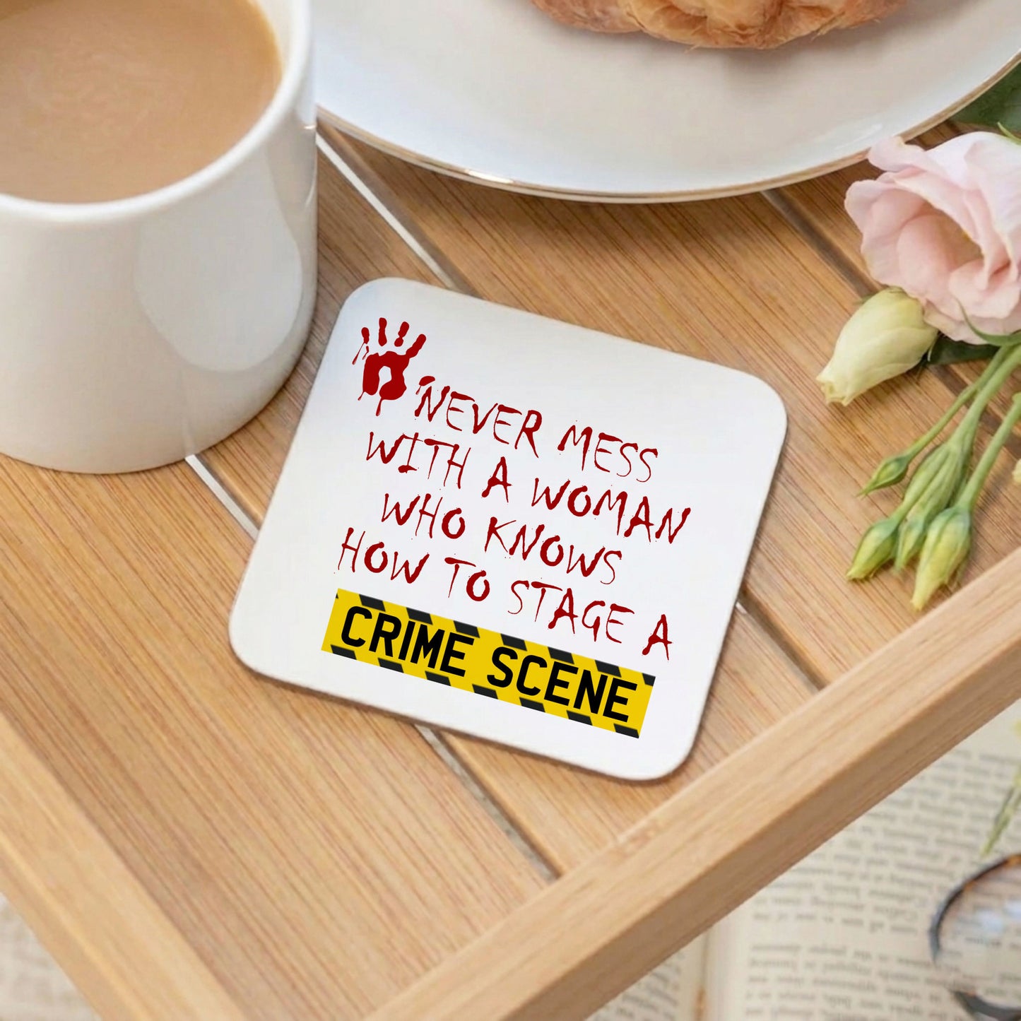 Coaster with humorous text on a wooden table with a cup of coffee and flowers.
