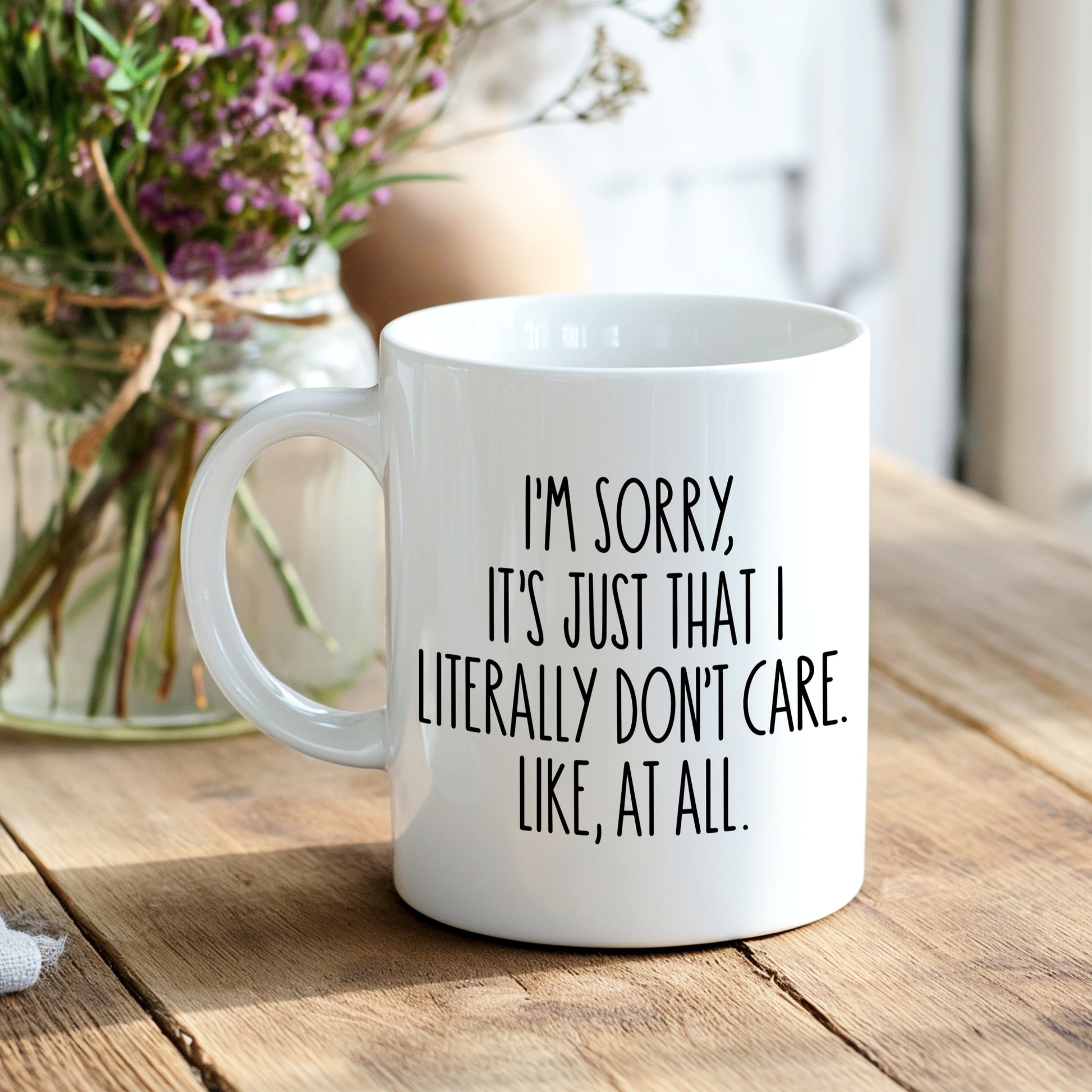 White mug with black text "I'm sorry, it's just that I literally don't care. Like, at all", on a breakfast table with a blurred background