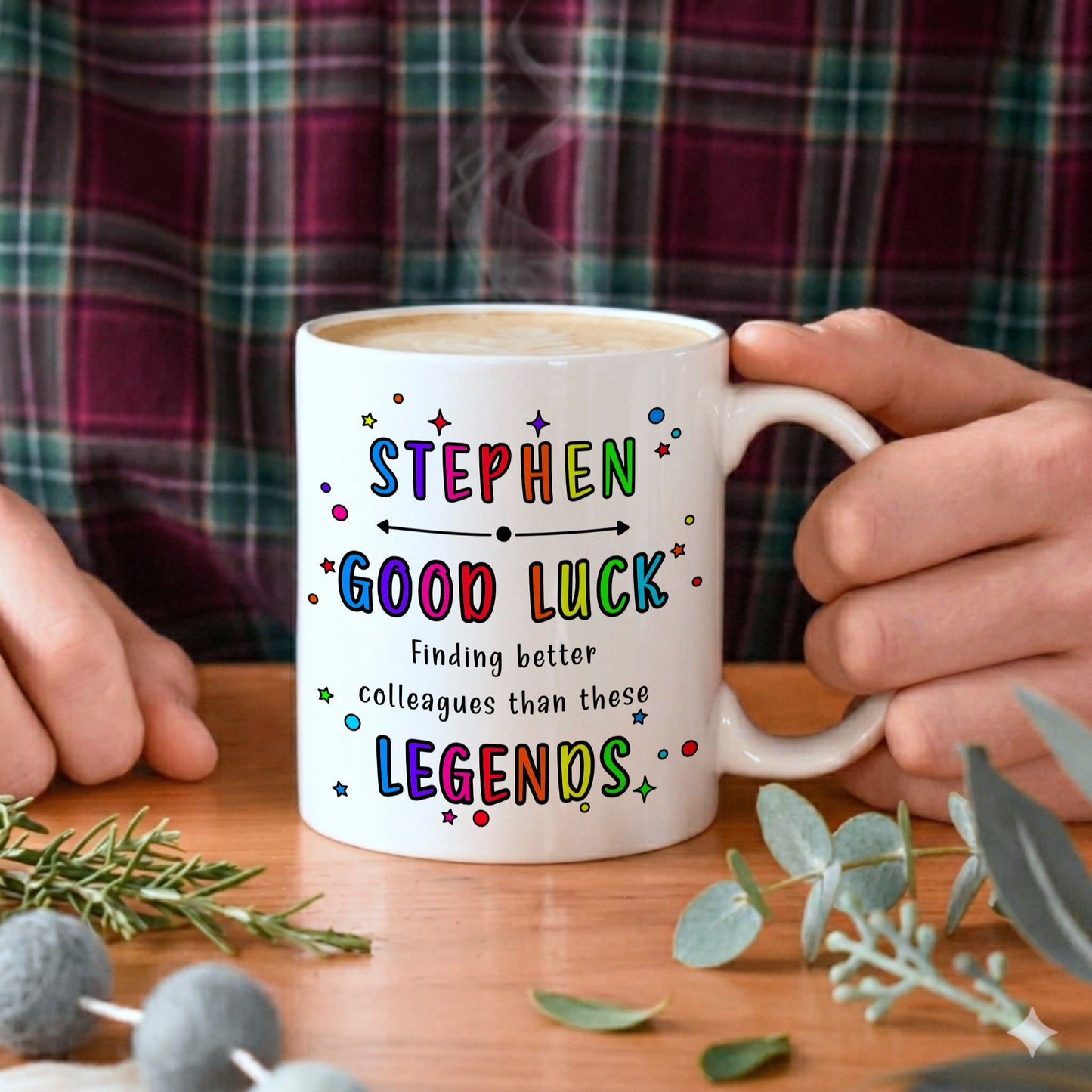 Person holding a mug with colourful text on a wooden table