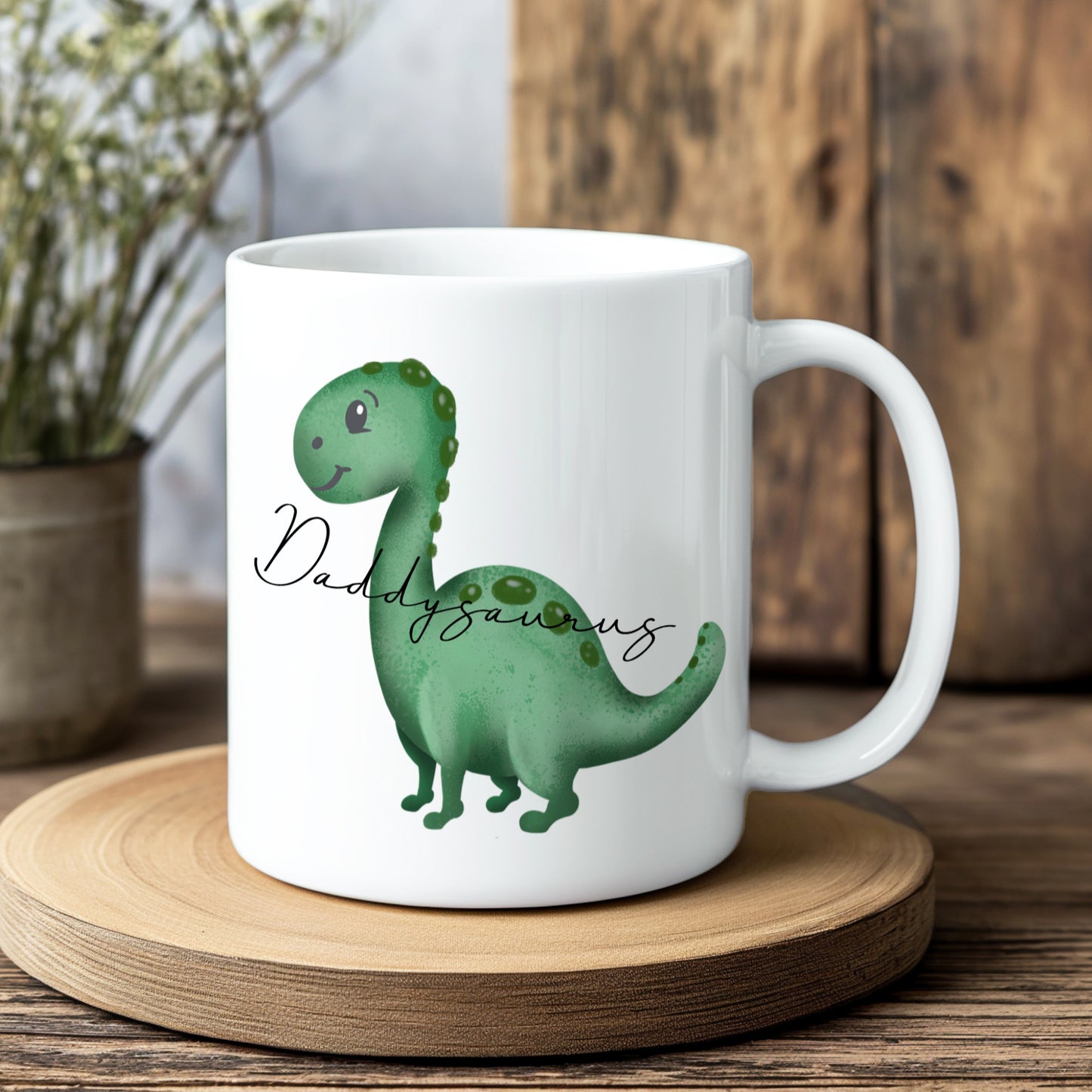 White mug with a green dinosaur illustration and 'Daddysaurus' text on a wooden coaster.