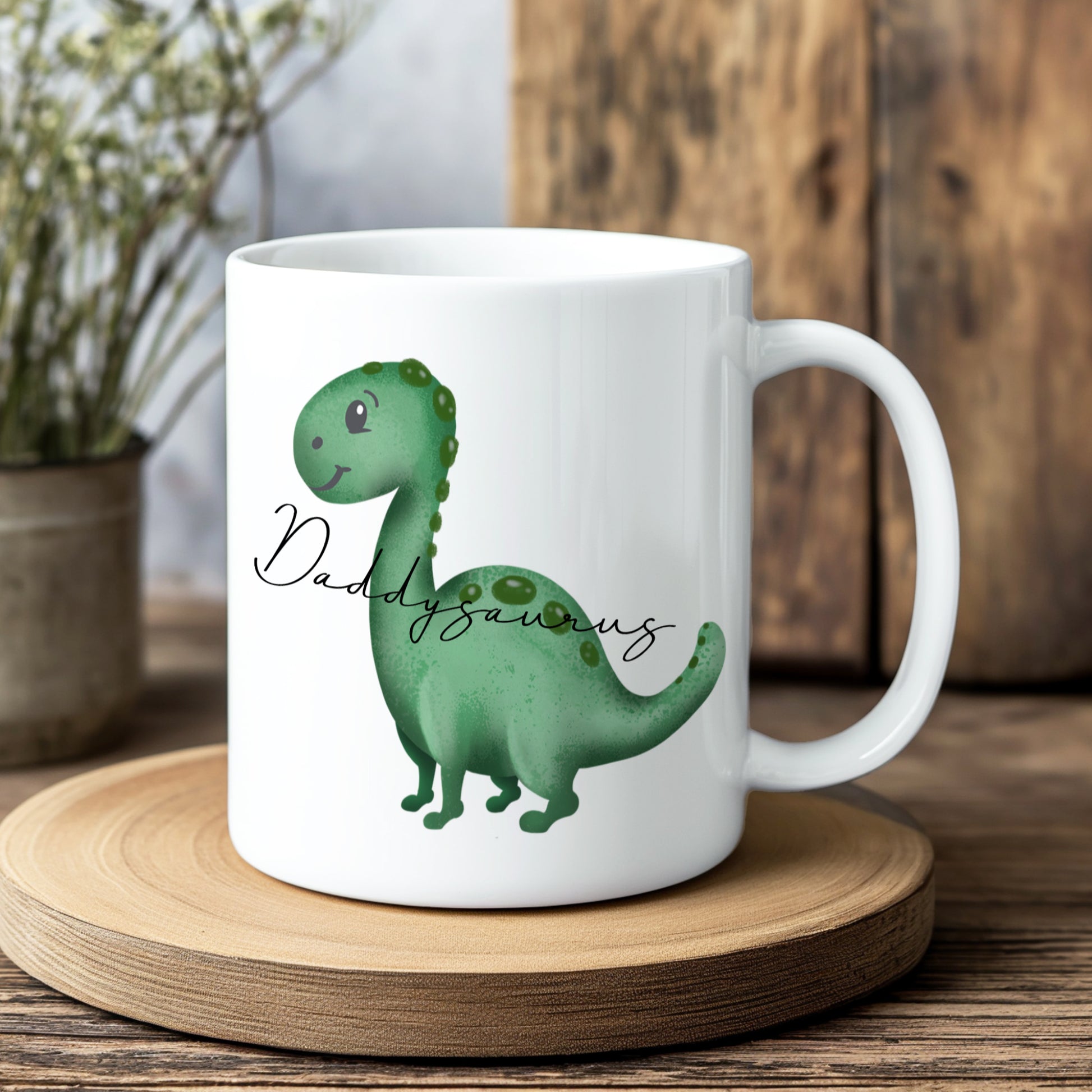 White mug with a green dinosaur illustration and 'Daddysaurus' text on a wooden coaster.