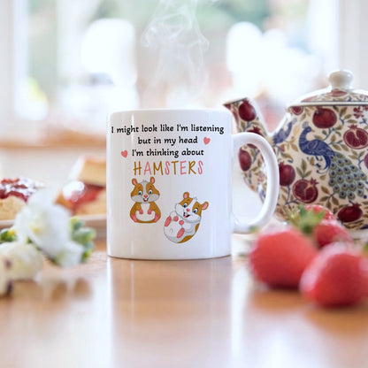 White mug with cartoon hamsters and text on a table with a teapot and strawberries.